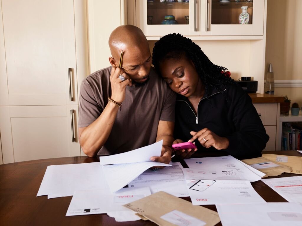 A couple sits at a table managing domestic finances, evaluating documents and using a smartphone