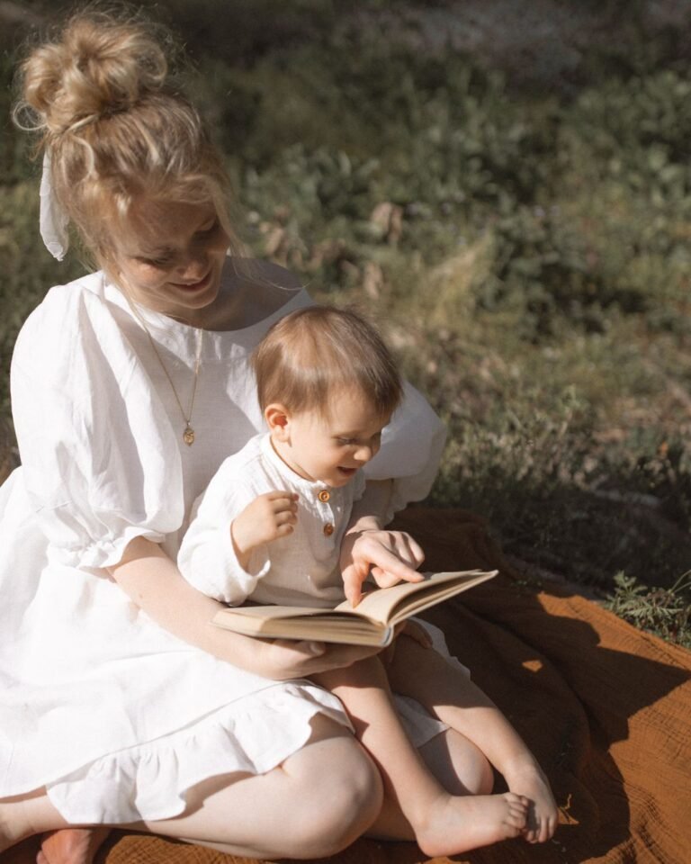 A mother and toddler enjoy reading together in a sunny outdoor setting.