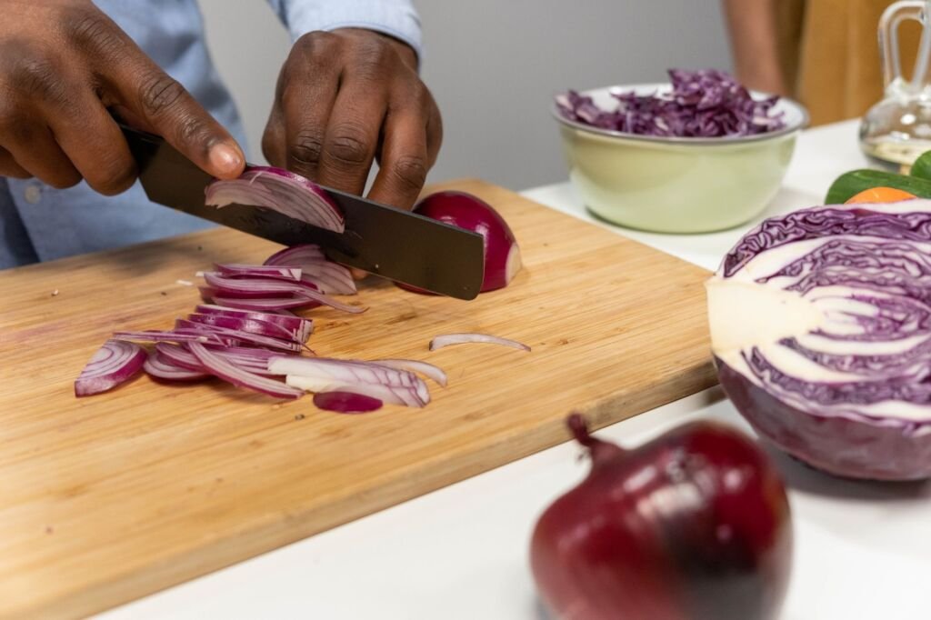 Close-up of hands slicing red onions on a wooden chopping board in a kitchen setting