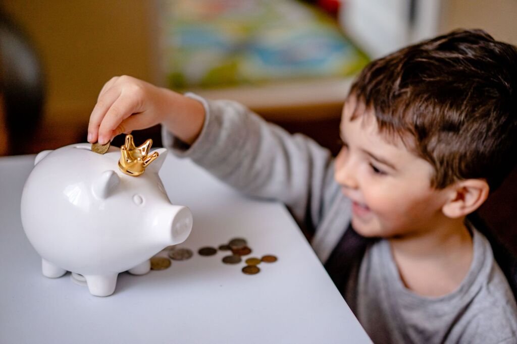 Young boy smiling while saving money in a crowned piggy bank, demonstrating financial responsibility