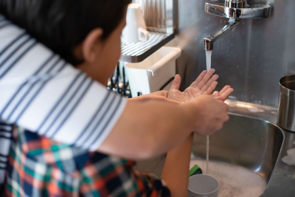 A child practicing hygiene by learning to wash hands under adult supervision at a kitchen sink