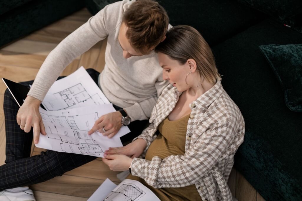 A couple sits on the floor reviewing house blueprints in their living room