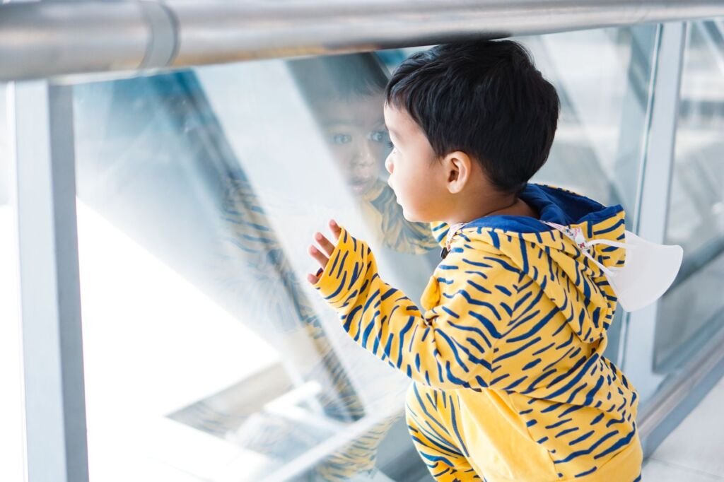 A cute little boy in a yellow tiger-print hoodie peers through a glass railing
