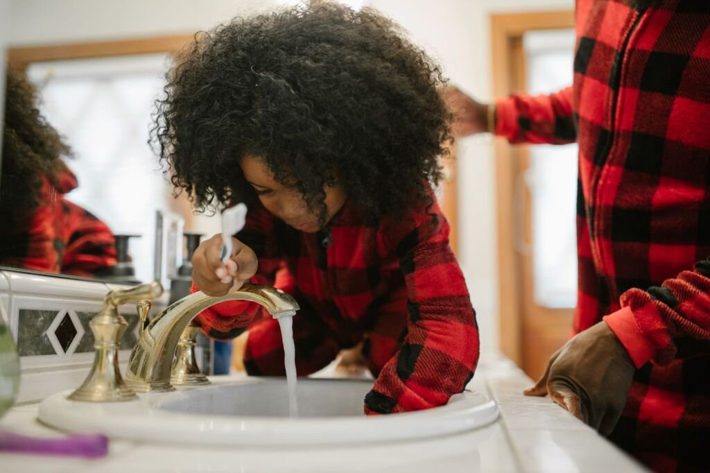 A father helps his daughter brush her teeth at the bathroom sink