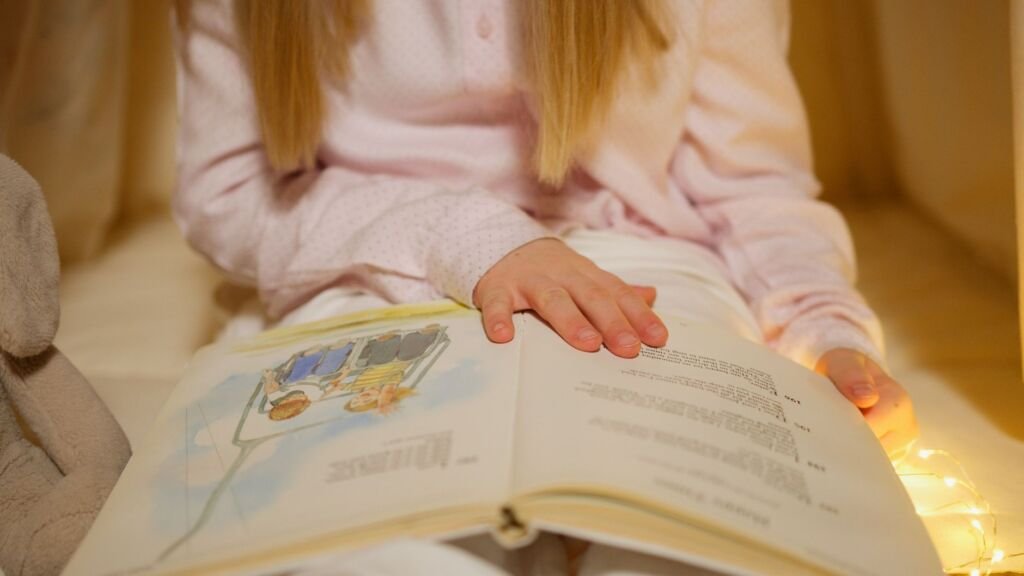 A young girl in pajamas reading a storybook in a warm, cozy bedroom setting