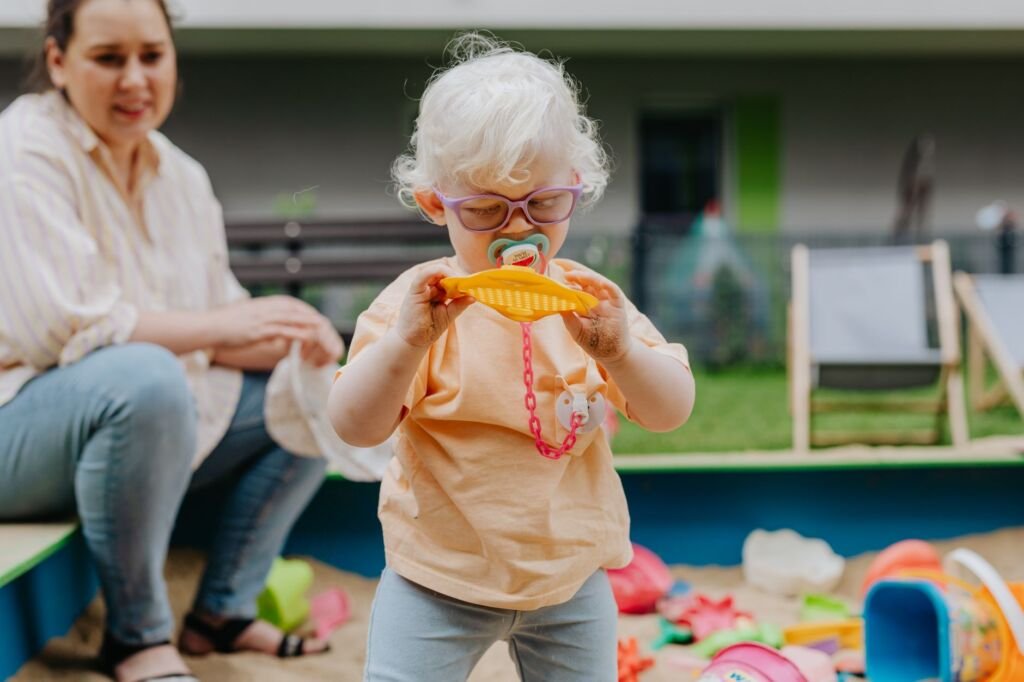 A young girl with glasses playing in a sandbox, exploring toys