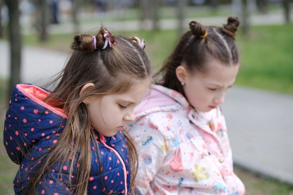 Two young girls in winter jackets, contemplative in a park setting