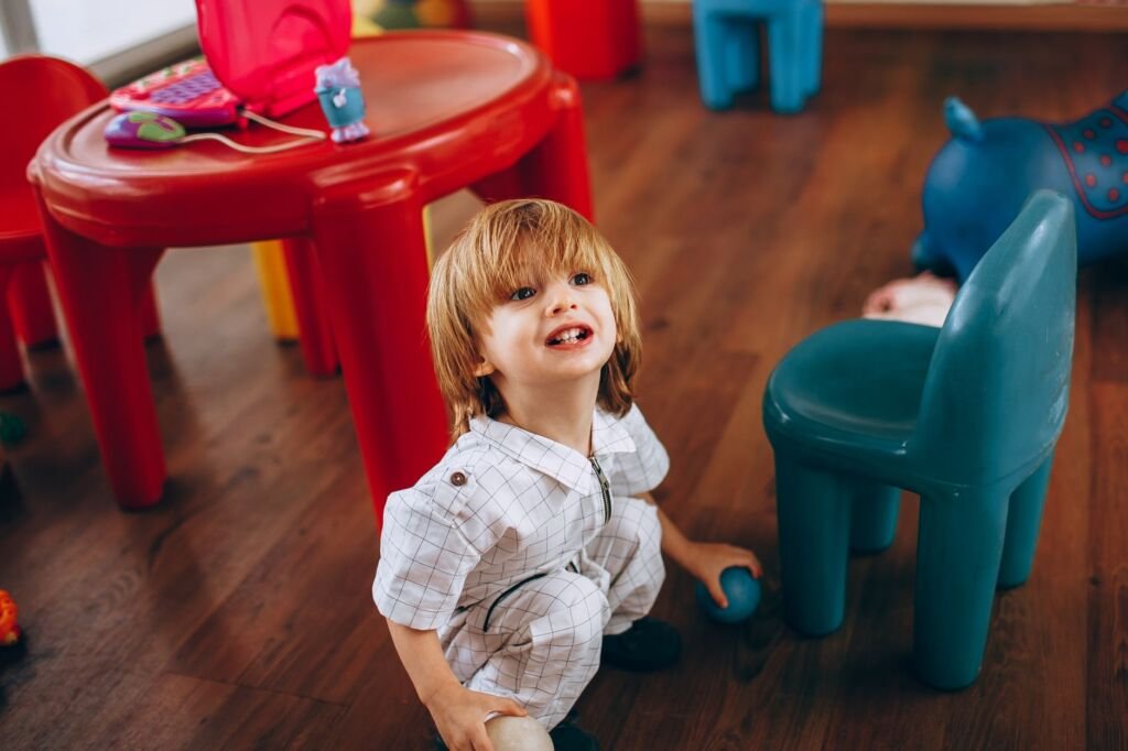 Young child in white outfit enjoying playtime in a vibrant indoor playroom with colorful toys